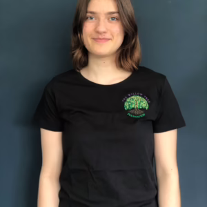 A young woman with light brown hair and a gentle smile wears a black t-shirt featuring The Willow Tree Foundation logo against a dark backgr