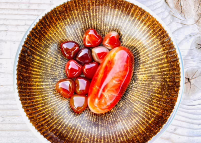 Shiny red and orange carnelian heart-shaped stones and a larger oval stone resting on a golden, patterned plate on wood.